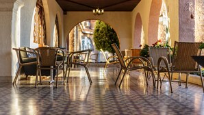 Un espace extérieur abrité, aménagé avec des chaises en osier et un sol carrelé, qui mène à une porte en arc de cercle.