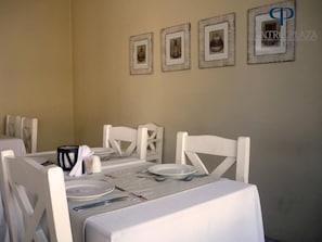 A dining area with a table set for four, white chairs, and framed pictures on the wall.