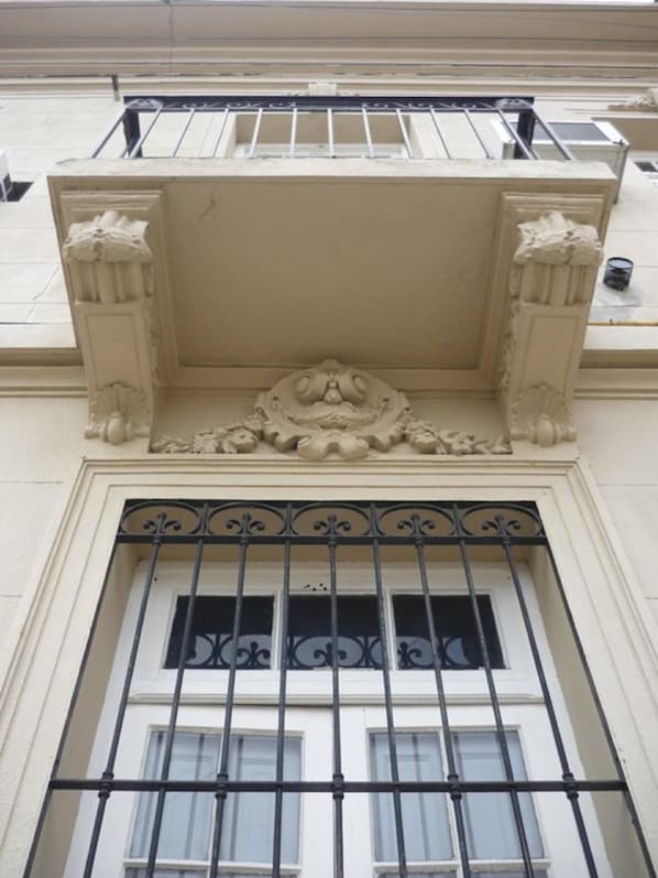A building facade with a decorative pediment, a balcony with wrought iron railings, and a window with barred glass.