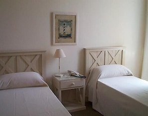 A hotel room with two single beds, a nightstand with a lamp, a framed picture on the wall, and a small table.