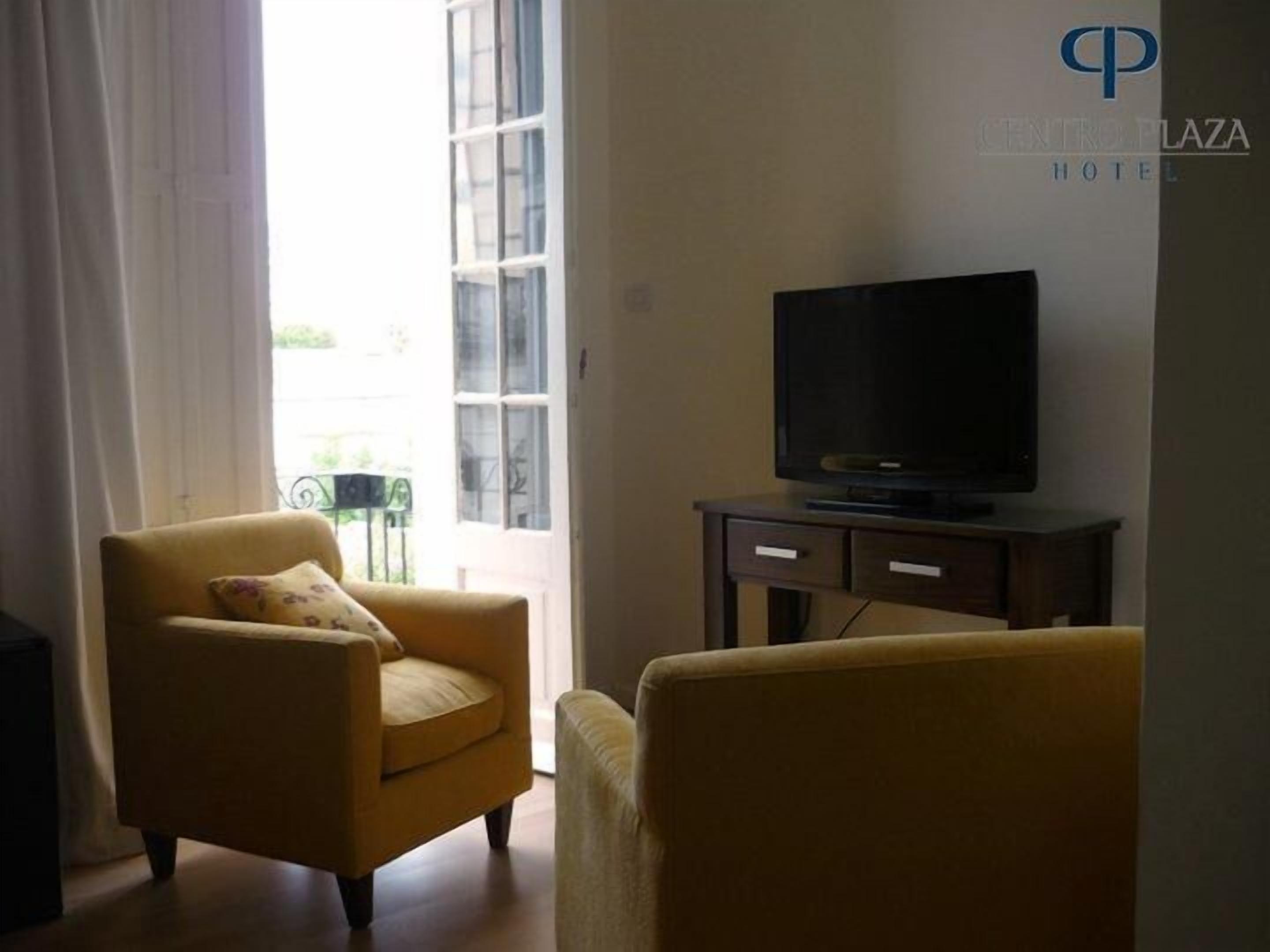 Una sala de estar con un sofá, un televisor sobre un mueble bajo y una ventana con cortinas.