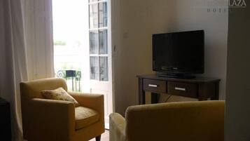 Una sala de estar con un sofá, un televisor sobre un mueble bajo y una ventana con cortinas.