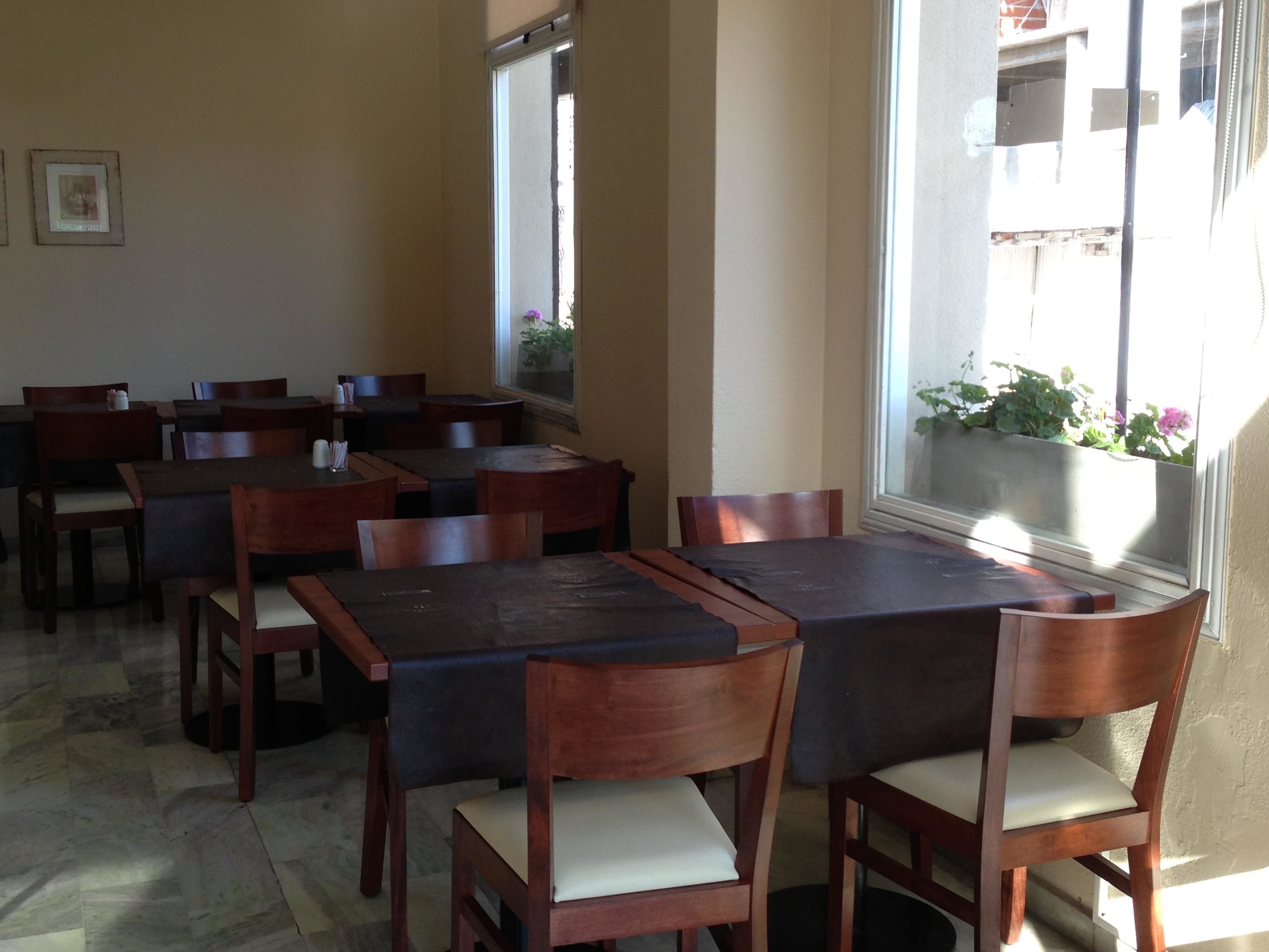 Un restaurante con mesas y sillas de madera, suelo de baldosas y una ventana con plantas.