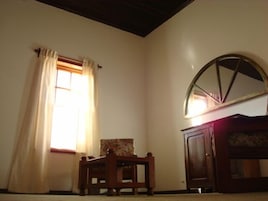 Una habitación con una silla de madera, un armario y una ventana con cortinas.