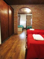 Habitación con dos camas, piso de madera y paredes de ladrillo.