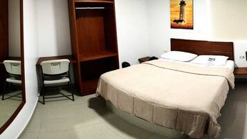 Una habitación de hotel con cama, escritorio, silla, armario y mesita de noche.