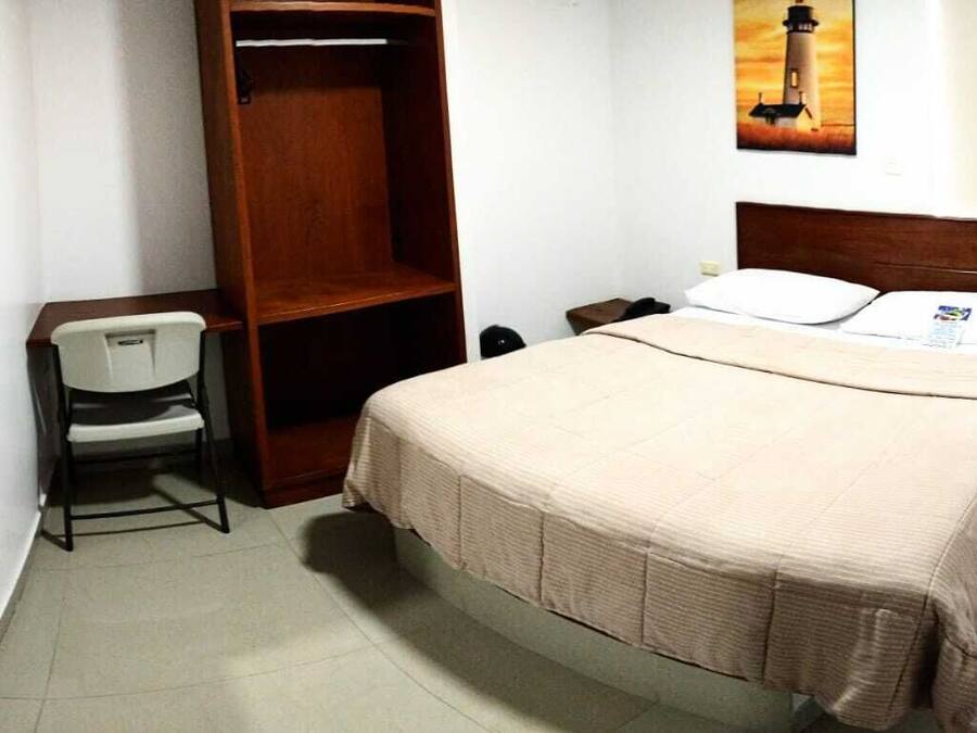 Una habitación de hotel con cama, escritorio, silla, armario y mesita de noche.