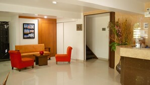 A modern reception area with a wooden door, a reception desk, a sofa, and two armchairs. - Hotel El Faro Buga (Guadalajara de Buga)