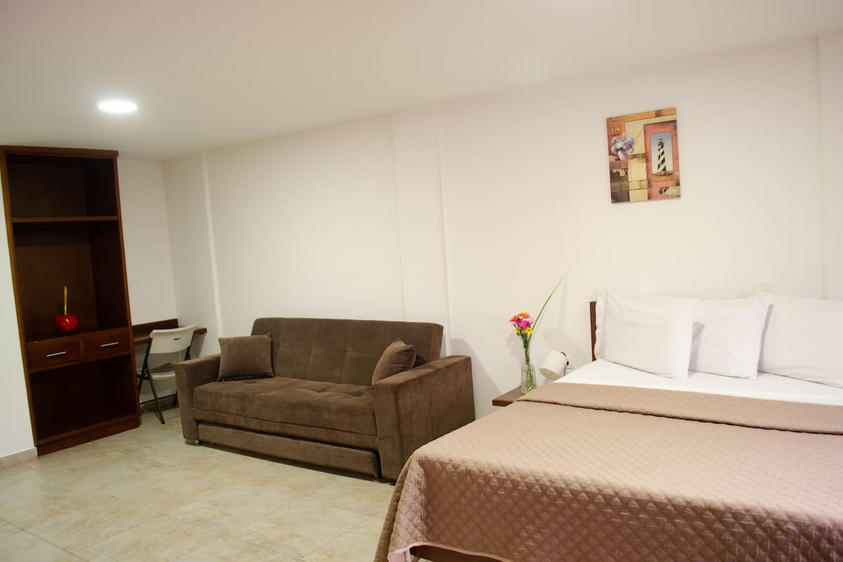 A hotel room with a bed, a brown sofa, a desk with a chair, and a wardrobe.