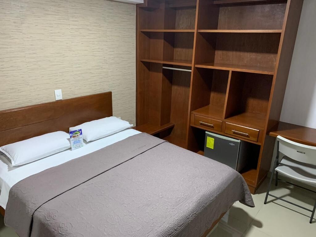 Ett hotellrum med en säng, en garderob i trä, ett skrivbord och en stol.