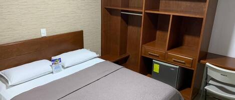 Ett hotellrum med en säng, en garderob i trä, ett skrivbord och en stol.