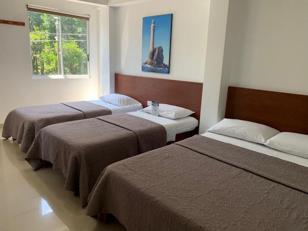 Habitación de hotel con tres camas, un ventanal grande y un cuadro de un faro.