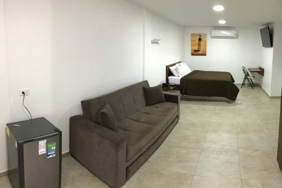 A compact hotel room with a sofa, a small desk, a bed, and a television.