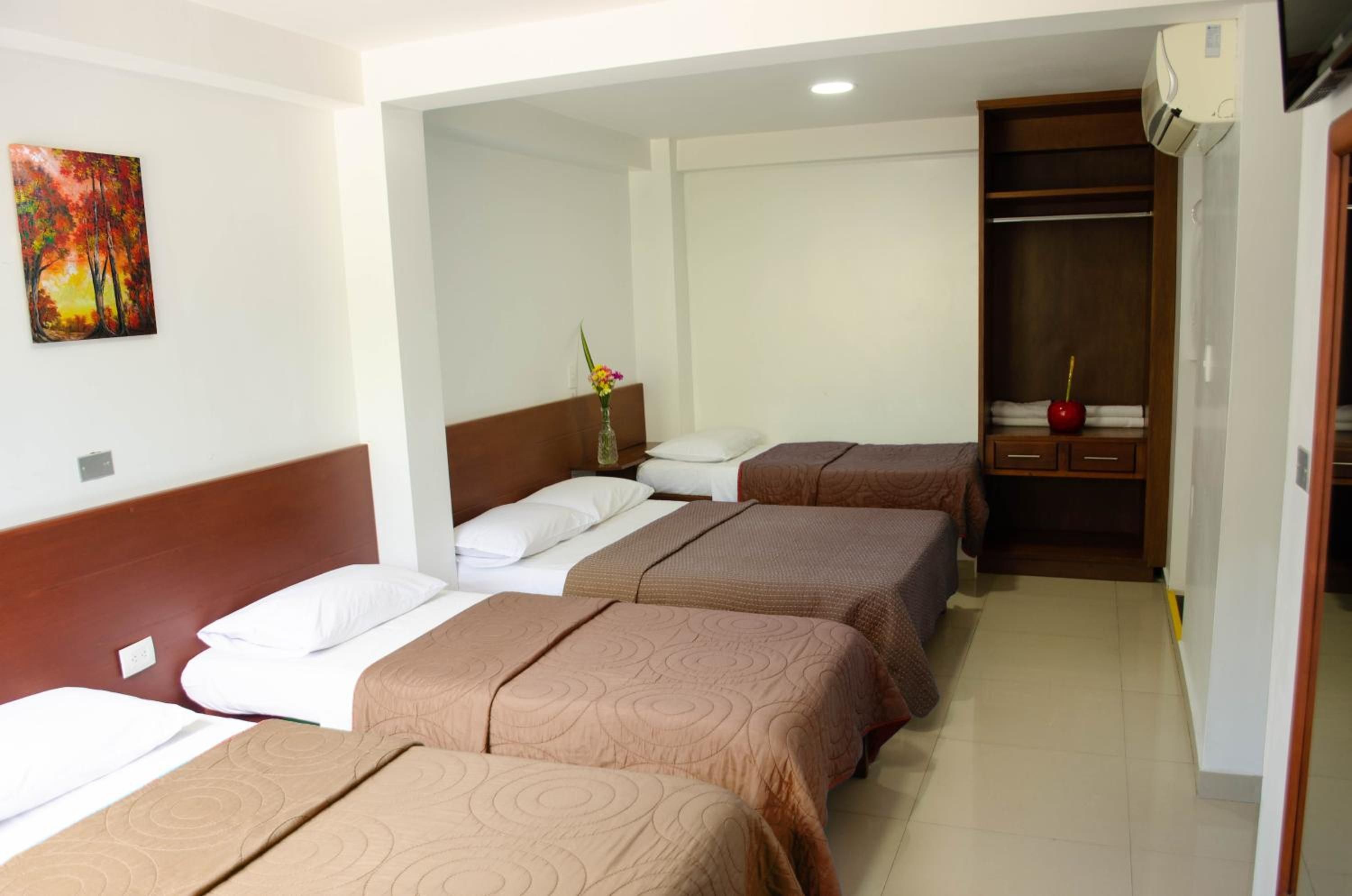 A hotel room with three beds, a wardrobe, and a painting on the wall.