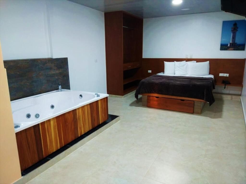 A room with a large bathtub, a bed with a wooden headboard, and a painting on the wall.