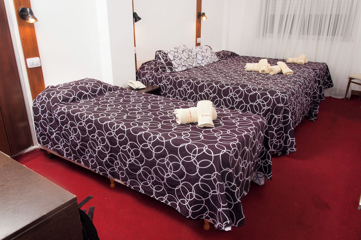 A hotel room with two beds, each with a patterned bedspread, a wooden headboard, a small bedside table, and a chair.