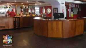 A hotel bar with wooden counters, a bartender, and a variety of liquor bottles. - Hotel Savoia (San Clemente)
