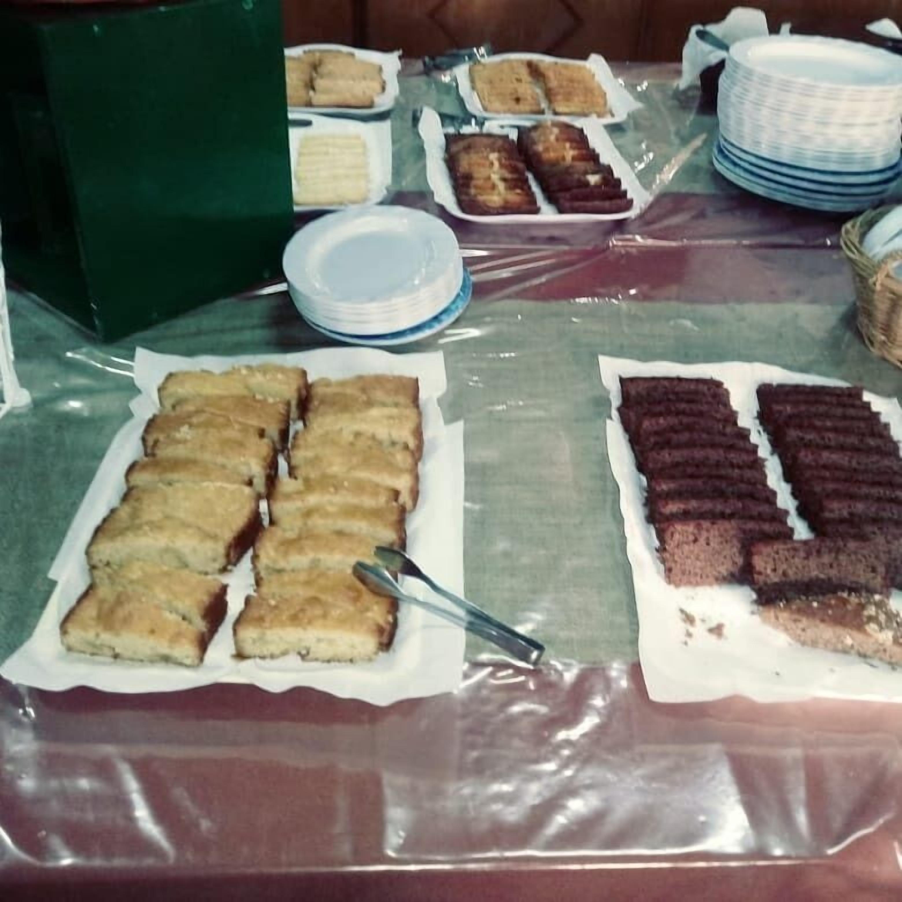A buffet table with various food items, including cakes and pastries, covered with plastic wrap.