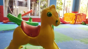 A yellow and green toy horse on a play mat with a window in the background. - Hotel Savoia (San Clemente)