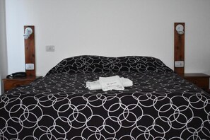 A neatly made bed with a black and white circular pattern bedspread, two bedside tables with lamps, and a folded towel on the bed.