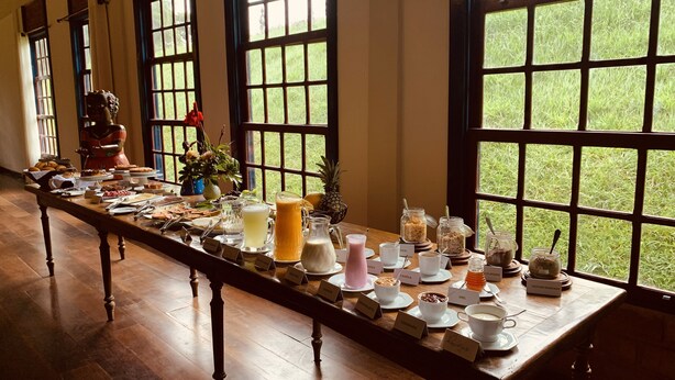 Un bufé de desayuno con diferentes alimentos y bebidas, dispuesto sobre una mesa larga con tarjetas de identificación.