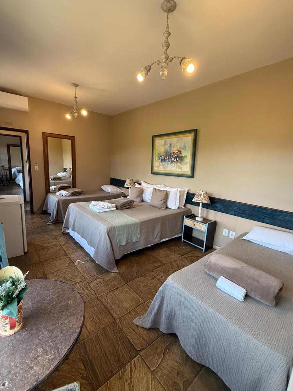 A hotel room with two beds, a small table, a chair, a lamp, and a painting on the wall.