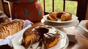 Uma mesa de sobremesas com diversos bolos e doces, um bule de chá e vista para a janela.