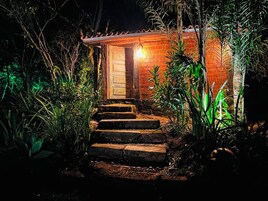 A brick building with a wooden door and steps leading up to it, surrounded by vegetation.