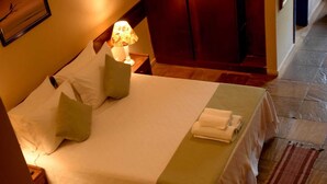 Una cama bien hecha con almohadas, una lámpara y una toalla doblada en el suelo de una habitación de hotel.