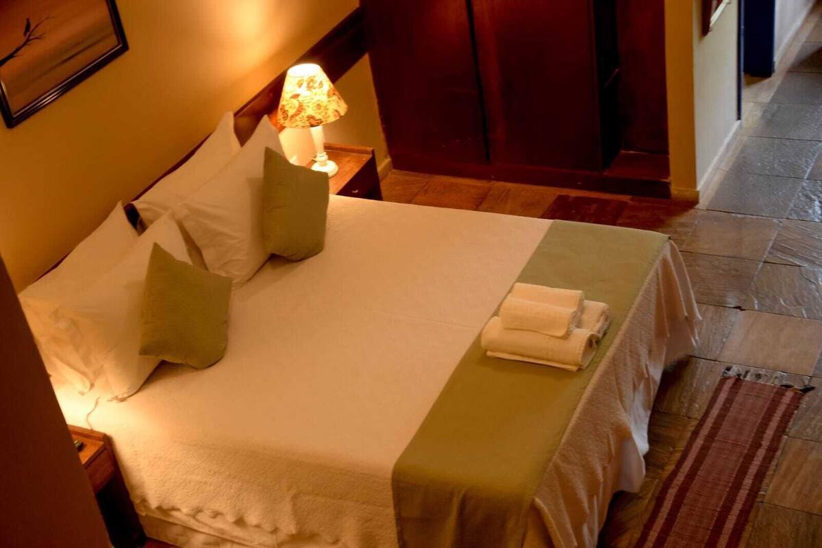 A neatly made bed with pillows, a lamp, and a folded towel on a hotel room floor.