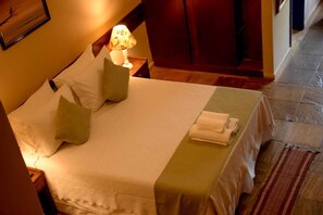 Una cama bien hecha con almohadas, una lámpara y una toalla doblada en el suelo de una habitación de hotel.