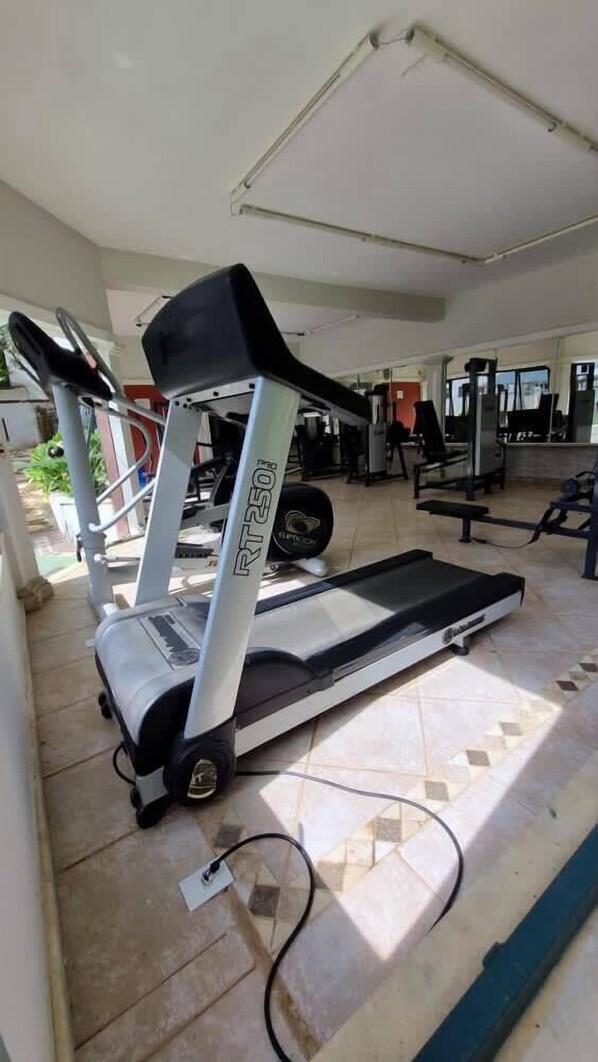 Un gimnasio con cinta de correr, equipo de ejercicio y piso de baldosas.