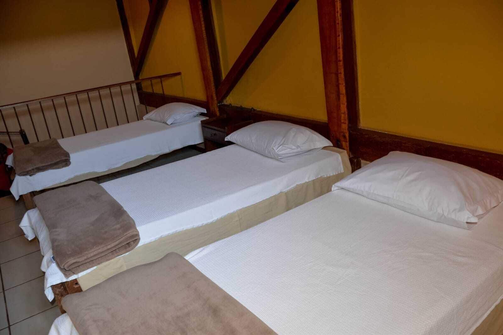 Una habitación con tres camas dispuestas en fila, vigas de madera en el techo y suelo de baldosas.