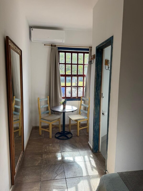A narrow hallway with a window, a table with two chairs, and an air conditioning unit. - Pousada Candonga Da Serra Hotel (Tiradentes)