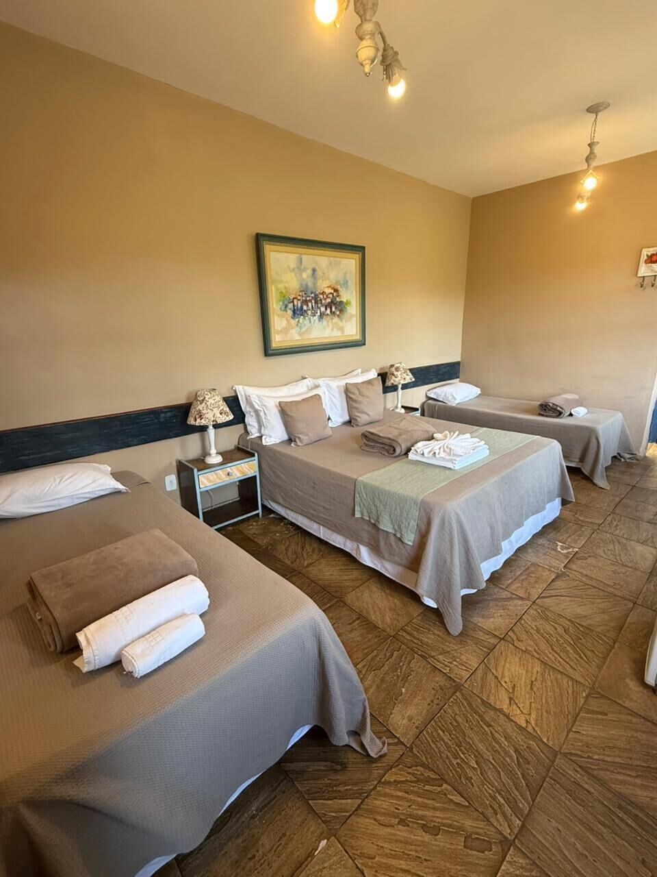 Una habitación de hotel con dos camas, un cuadro en la pared y piso de baldosas.