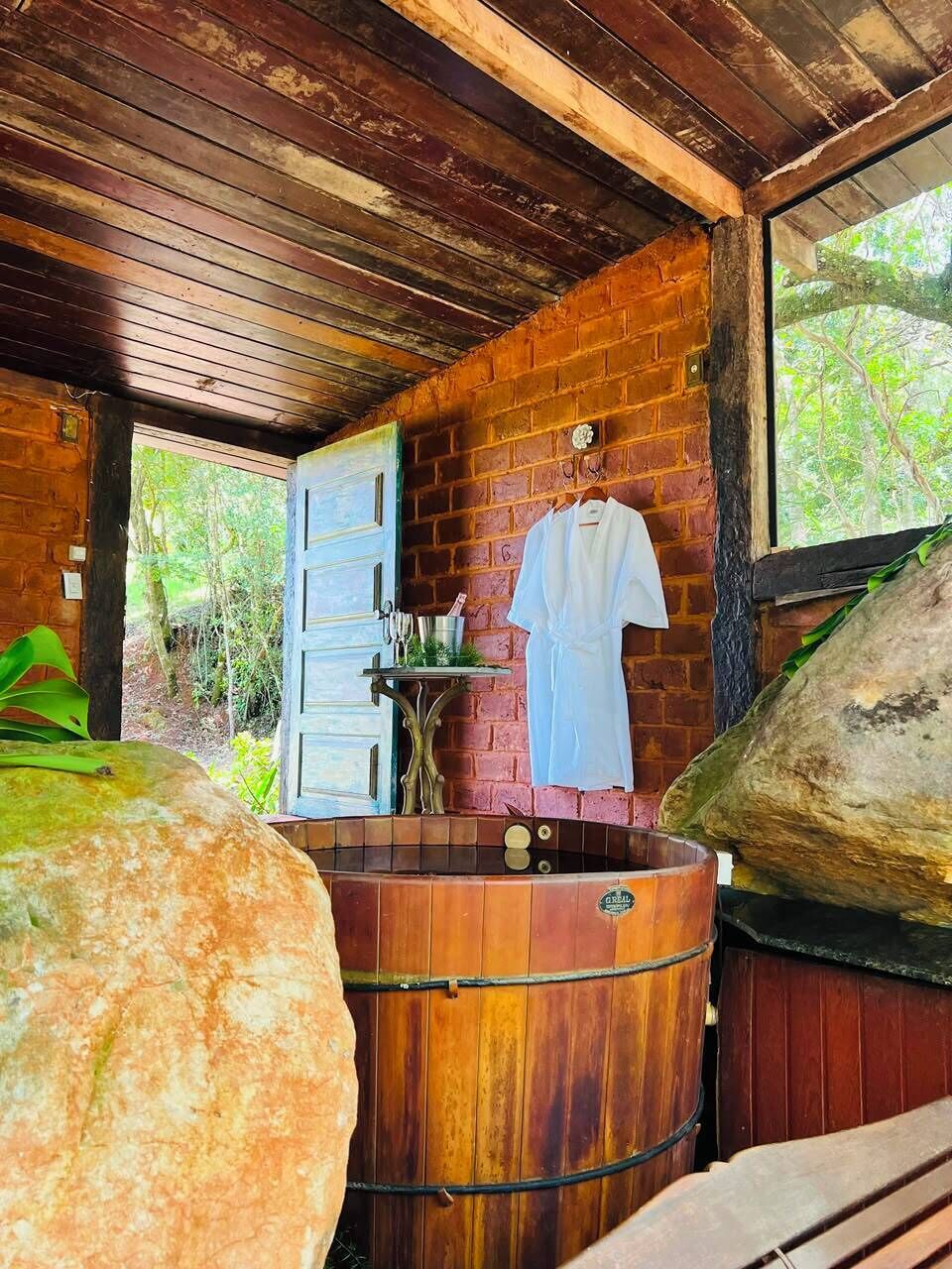 A rustic cabin with a wooden interior, a large hot tub, and a white robe hanging on the wall.