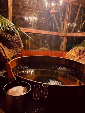 A hot tub with a wooden frame, a window with a view of trees, and a chandelier. - Pousada Candonga Da Serra Hotel (Tiradentes)