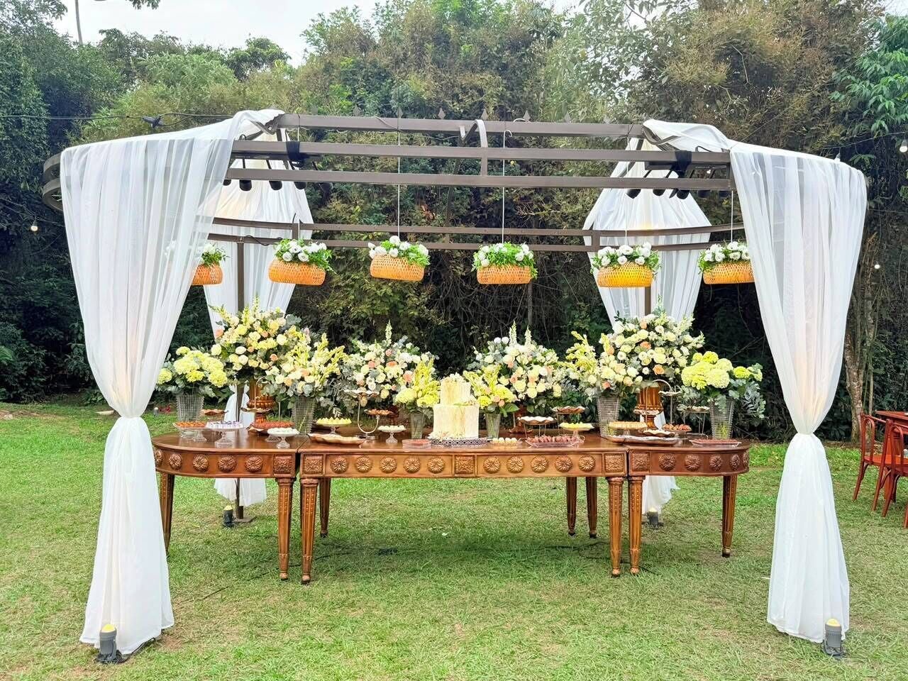 Montaje para un evento al aire libre con una mesa decorada con arreglos florales y una estructura de toldo.