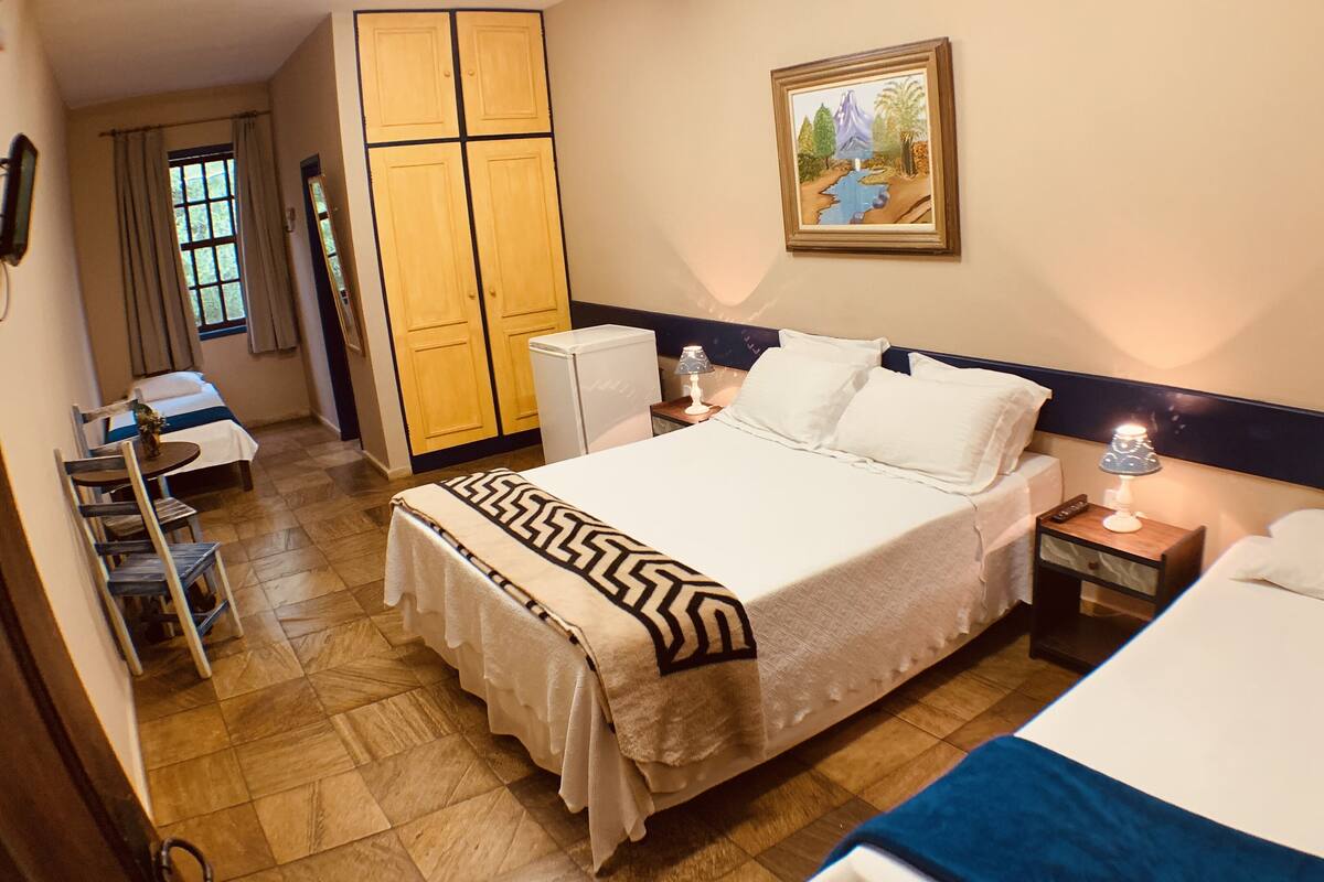 A hotel room with a large bed, a smaller bed, a desk, a wardrobe, and a painting on the wall.