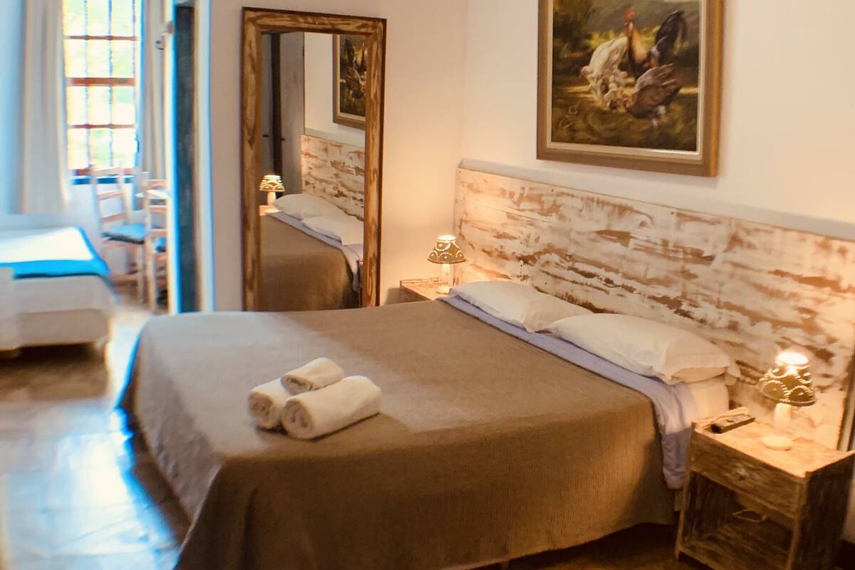 A hotel room with a large bed, a bedside table with a lamp, a mirror, and a painting on the wall.