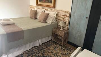 A bedroom with a bed, pillows, a nightstand with a lamp, a patterned rug, and a wardrobe.