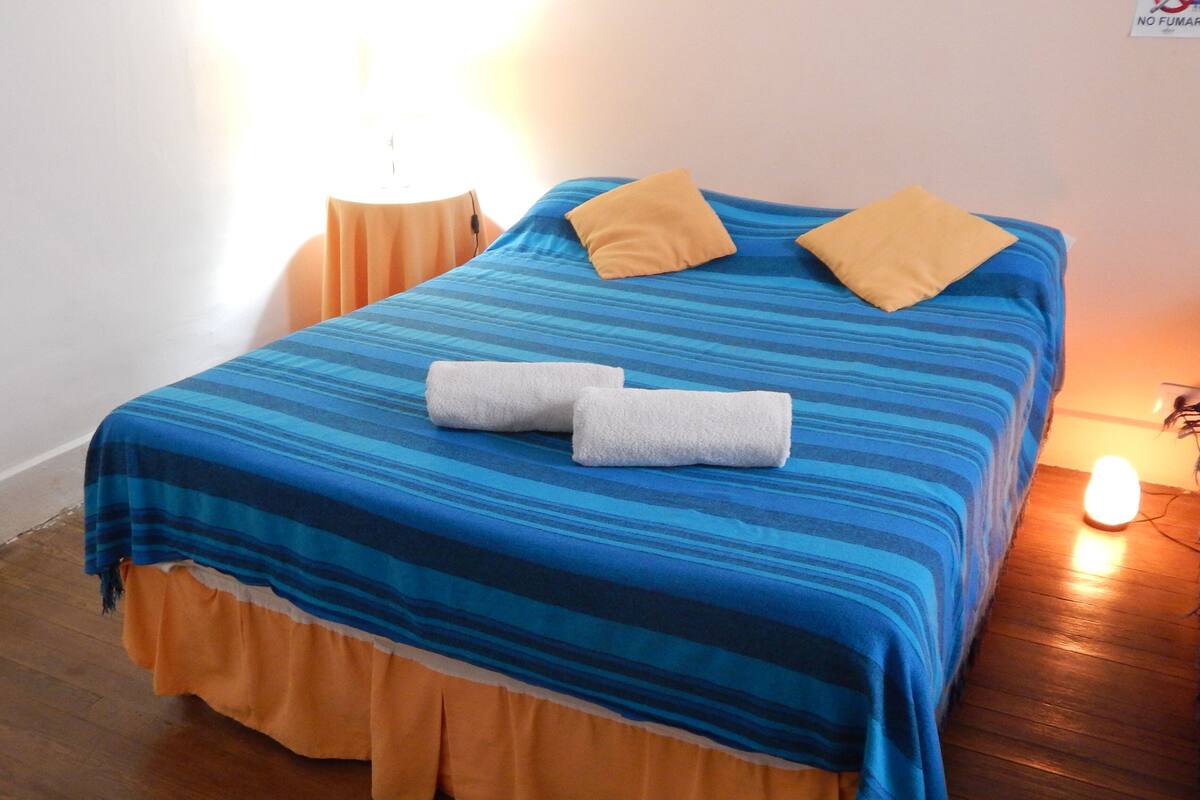 Un lit avec une couvre-lit à rayures bleues et oranges, deux oreillers et deux serviettes enroulées.