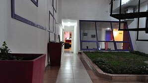A hallway with a tiled floor, a potted plant, and a window with a view of a building in the background. - Altea Hotel de Rosario (Rosario)