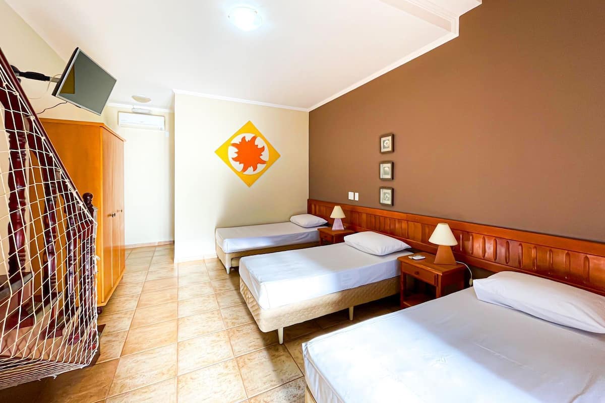 A hotel room with three single beds, a TV mounted on the wall, and a wooden staircase.