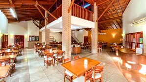 Un vaste espace dédié à la salle à manger, avec de nombreuses tables et chaises en bois, une structure en colonnes de briques et un haut plafond également en bois.