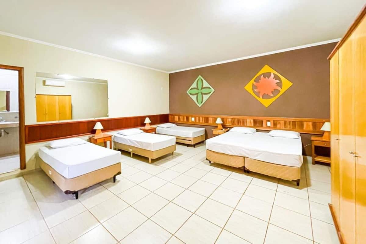 A hotel room with four beds, a wooden wardrobe, a mirror, and a wall with decorative symbols.