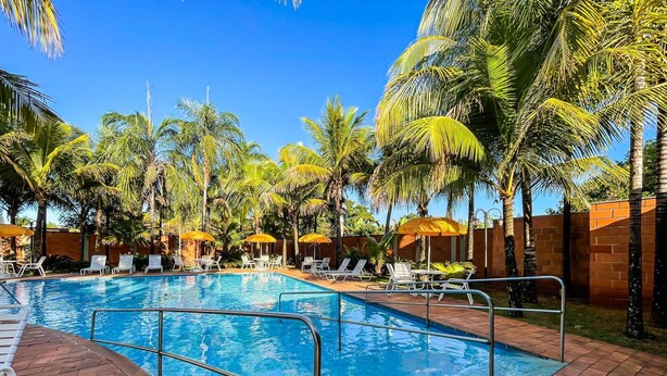 Une piscine entourée de palmiers, avec des chaises longues et des parasols.
