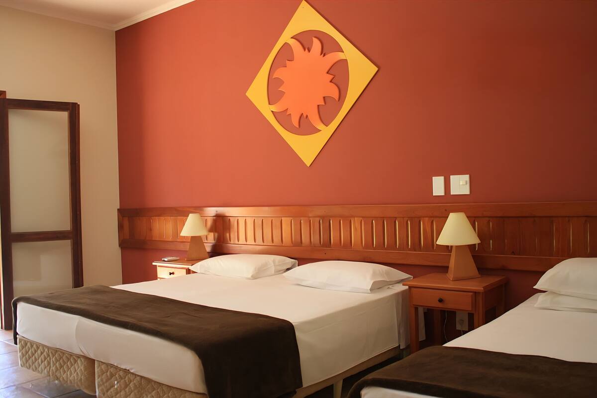 A hotel room with two beds, wooden headboards, bedside tables with lamps, and a large decorative wall piece.