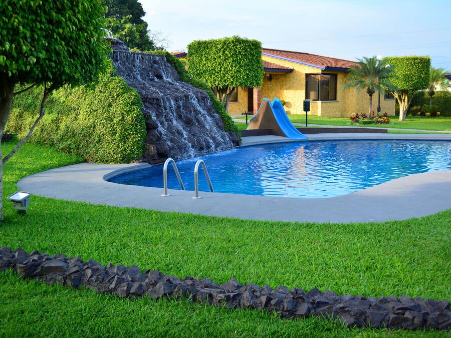 Una piscina con cascada, rodeada de césped cuidado y un borde de piedra.