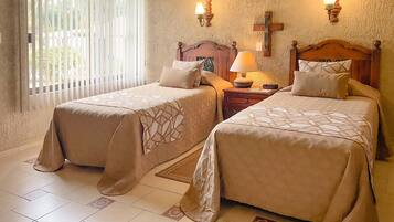A hotel room with two beds, a wooden headboard, a nightstand with a lamp, and a window with blinds.